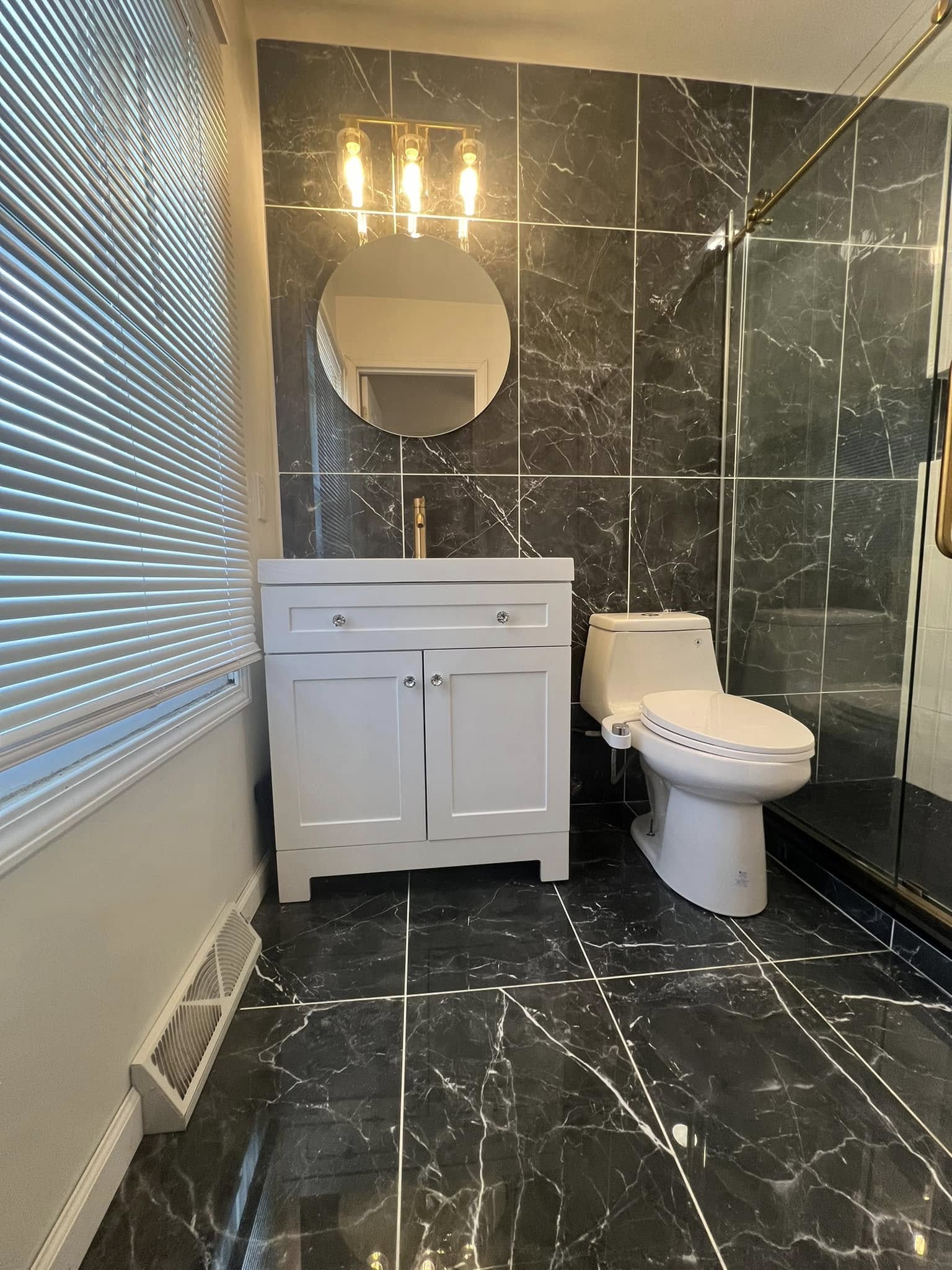 Custom bathroom remodel with black marble tile, brass fixtures, and glass shower