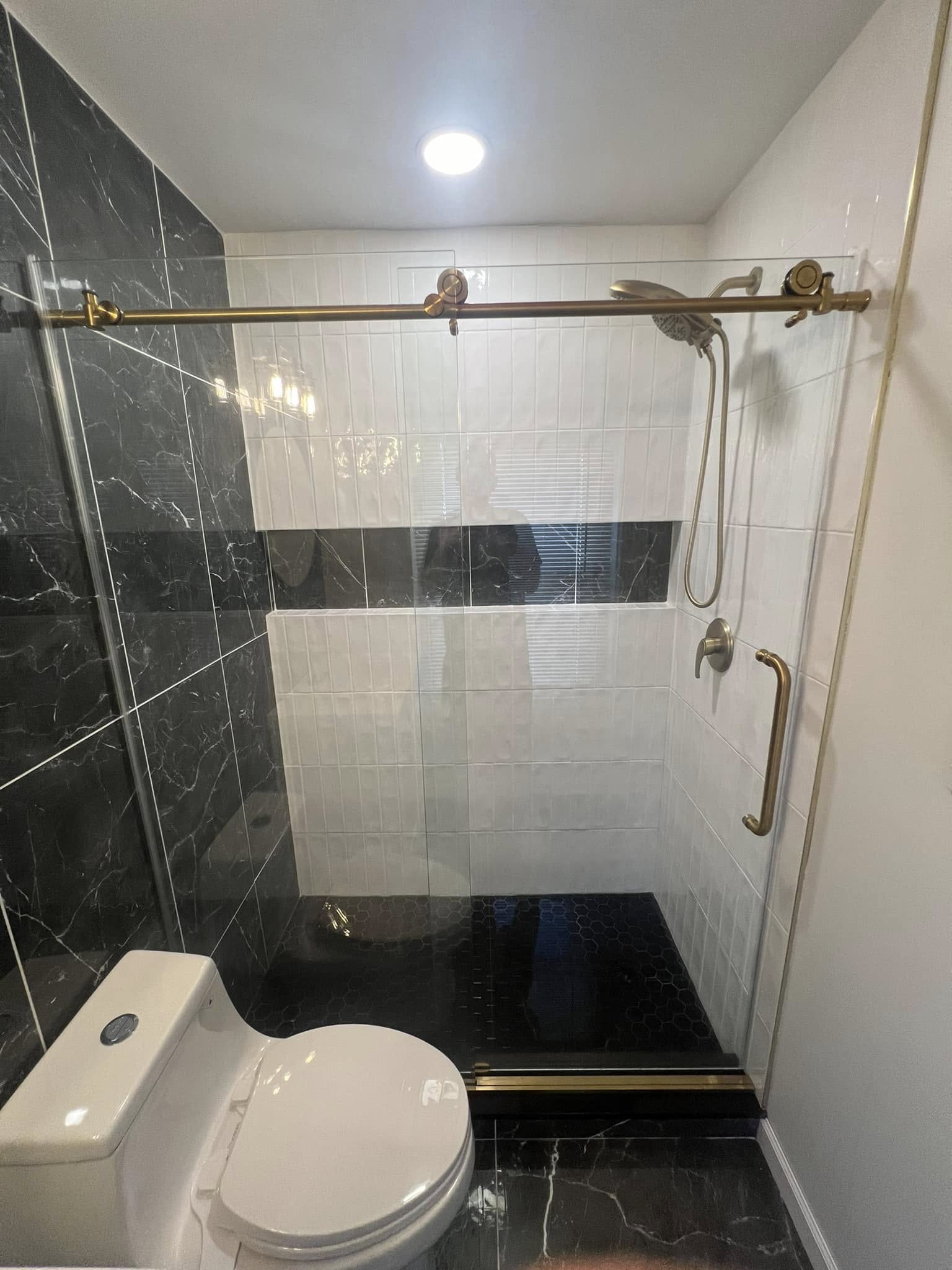 Black marble and white tile shower with frameless glass door